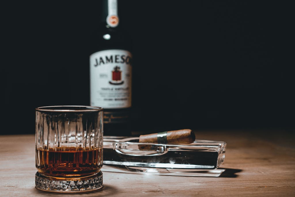 Elegant scene of whiskey glass and cigar on a wooden table with a bottle in the background.